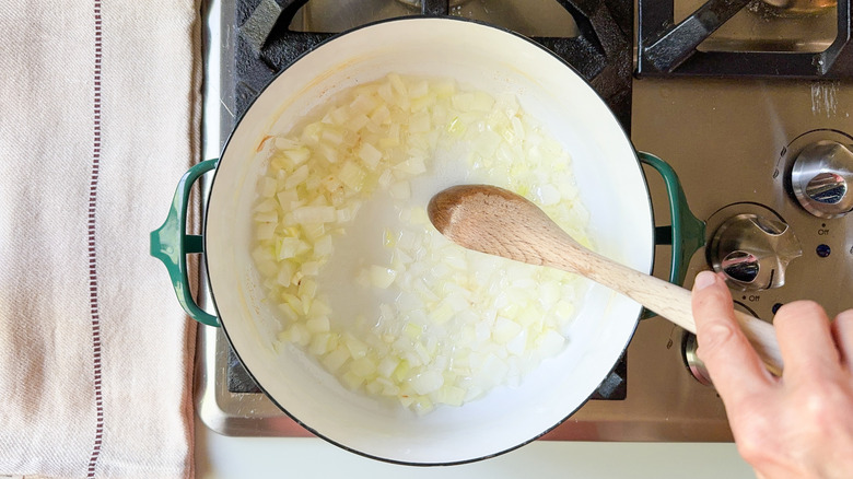 Sauteing onion and garlic in pot on stovetop with wooden spoon