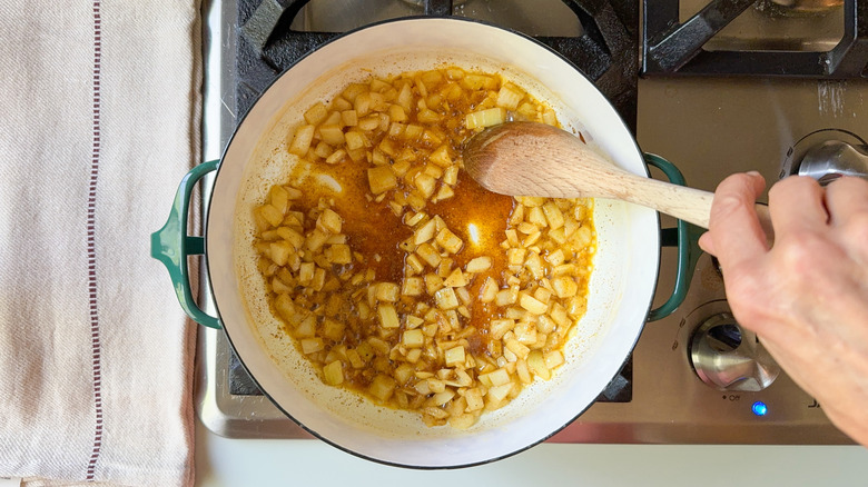 Sauteing garlic and onion with spices in pot on stovetop with wooden spoon