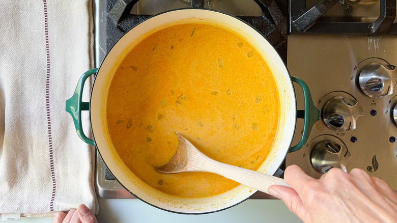 Stirring canned pumpkin and coconut milk into spooky pumpkin curry Halloween soup