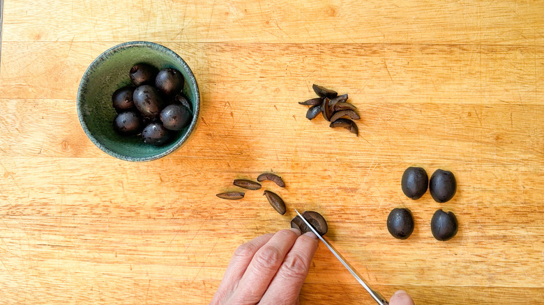 Cutting pitted black olives into strips on cutting board