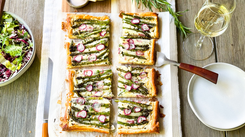 Springy asparagus and lemon ricotta tart on serving platter on table with wine and salad