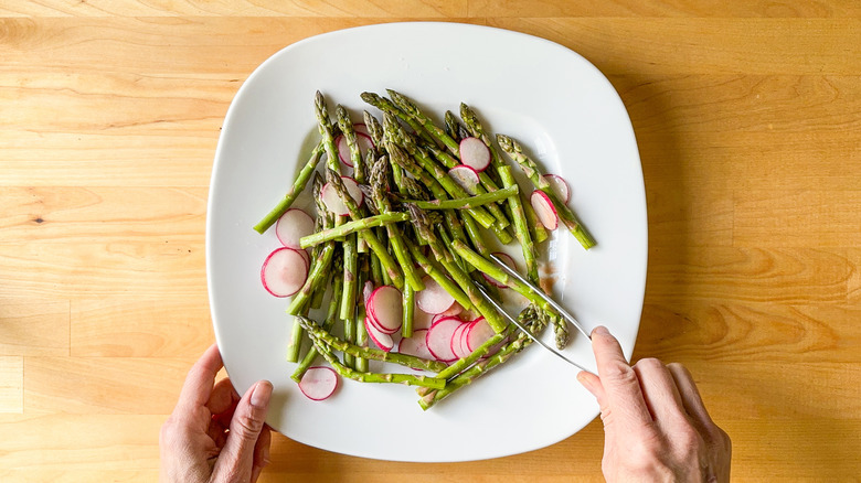 Asparagus spears and radish slices being tossed with olive oil and salt