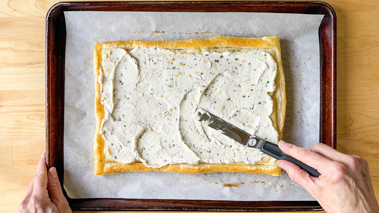 Spreading lemon ricotta filling over baked puff pastry with offset spatula on baking sheet