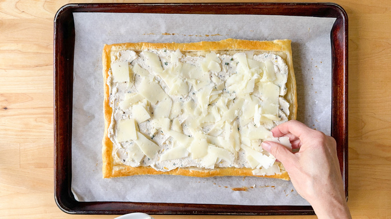 Layering shaved manchego over lemon ricotta filling on puff pastry on parchment-lined baking sheet
