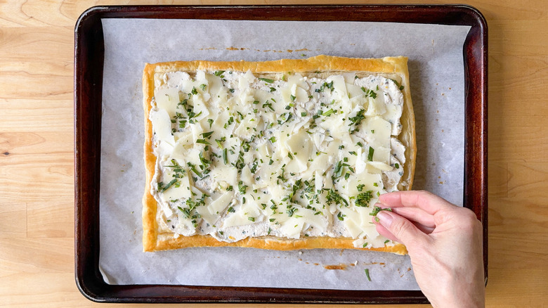 Sprinkling fresh chopped tarragon over shaved manchego on baked puff pastry on baking sheet