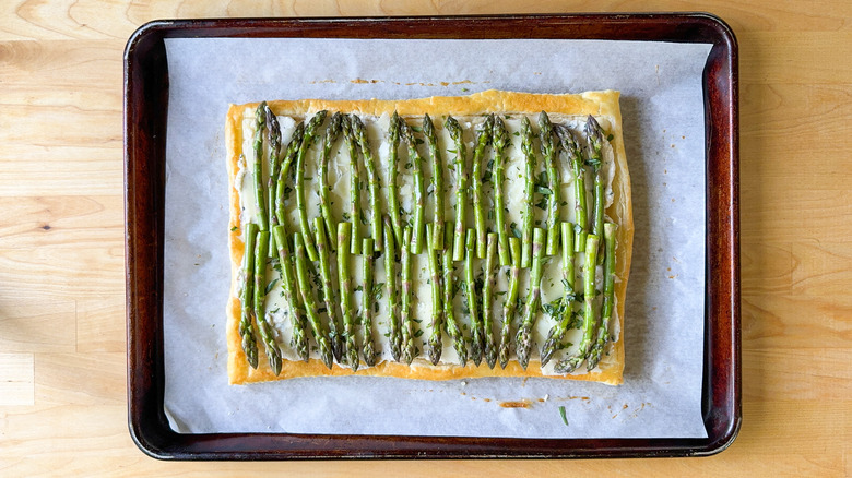 Rows of asparagus on baked puff pastry with lemon ricotta, manchego, and tarragon on baking sheet