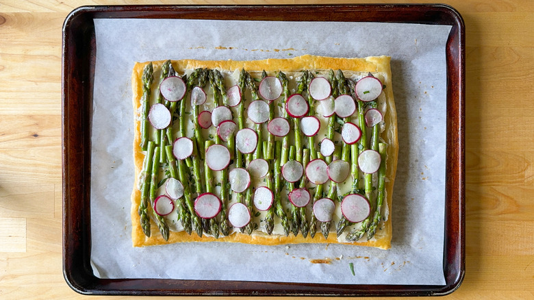 Sliced radishes and asparagus spears on lemon ricotta filled puff pastry on baking sheet