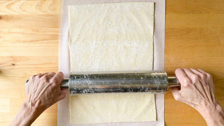 Rolling out puff pastry on parchment paper with rolling pin