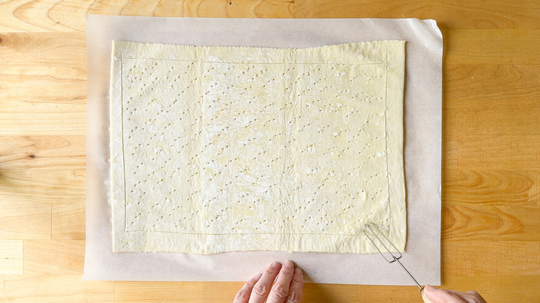 Using a fork to prick puff pastry on parchment paper
