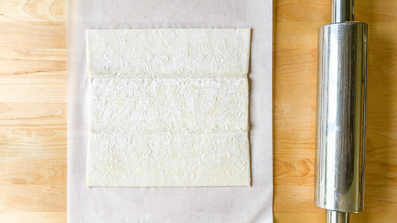 Sheet of puff pastry on parchment paper with rolling pin