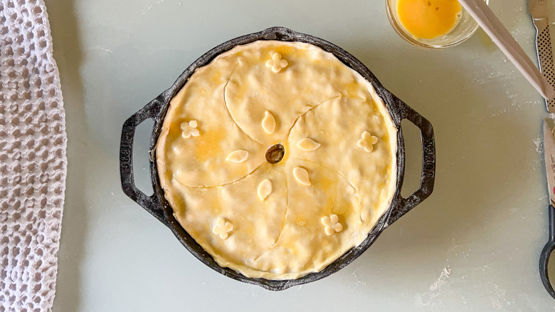 Unbaked springy vegetarian pot pie in cast iron skillet with decorative puff pastry crust