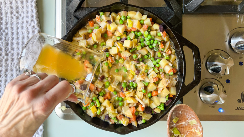 Adding vegetable stock to pot pie vegetables in cast iron skillet on stove top