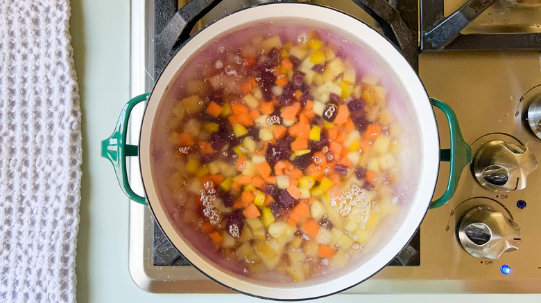 Pot with diced multi colored carrots and potatoes in water on stove top