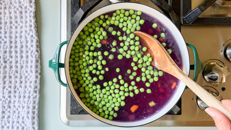 Peas in pot of water with carrots and potatoes with wooden spoon on stove top