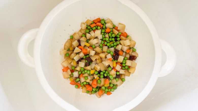 Peas, diced potatoes and carrots in colander in sink