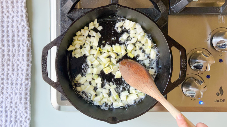 Diced fennel bulb cooking in butter in cast iron skillet on stove top