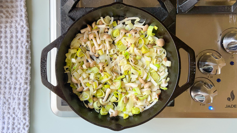 Leeks, beech mushrooms, fennel and garlic cooking in cast iron skillet on stove top