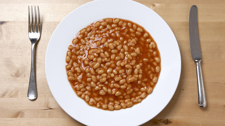 A bowl of baked beans on a table with a fork and knife