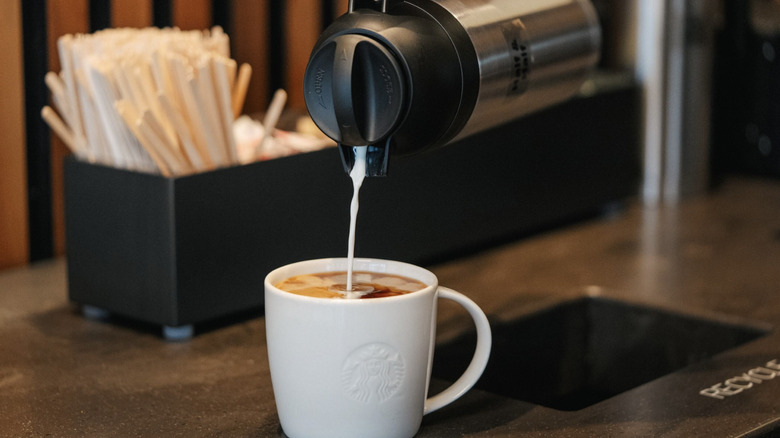 Creamer pouring into a white Starbucks mug of coffee