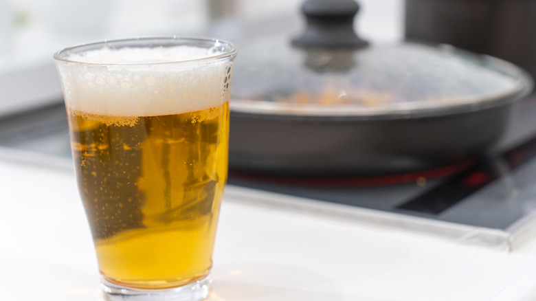 A glass of light beer sits on a kitchen counter near a pot on a stove.
