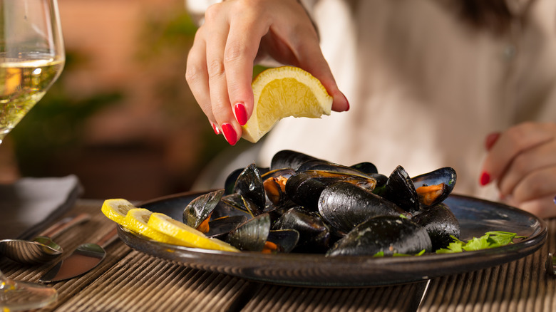 A person's hand squeezes a lemon wedge over a plate of steamed mussels.
