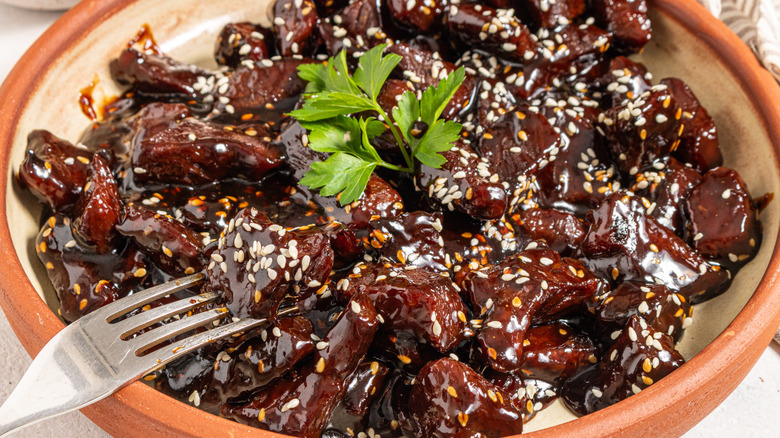 Fork leaning on a plate over sticky soy steak bites garnished with sesame seeds and fresh parsley 