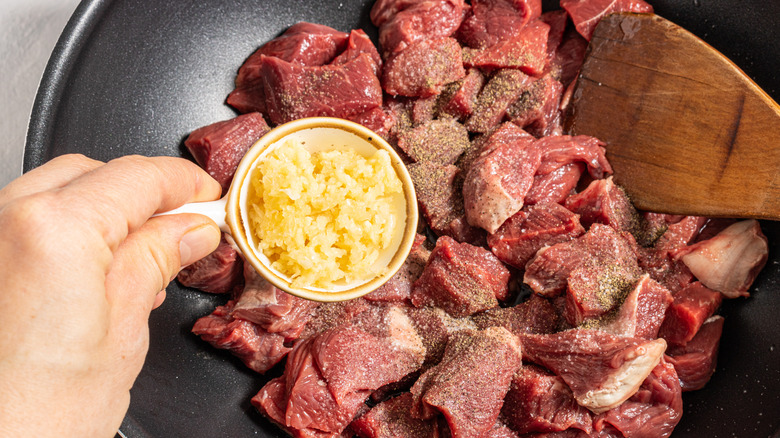 Adding minced garlic to pan with steak pieces