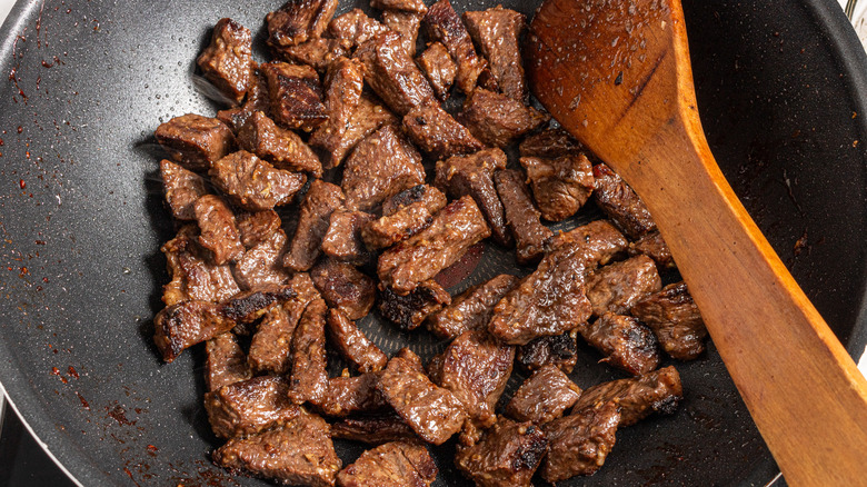 cooked steak pieces in wok pan with wooden spoon