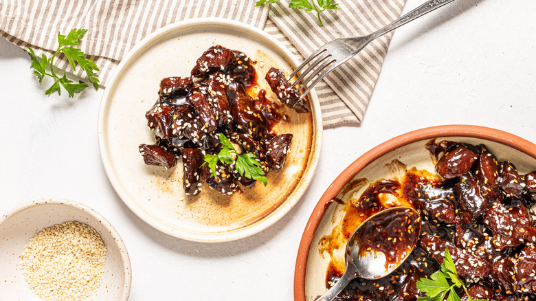 Plates with sticky soy steak bites, a fork, and a bowl with sesame seeds