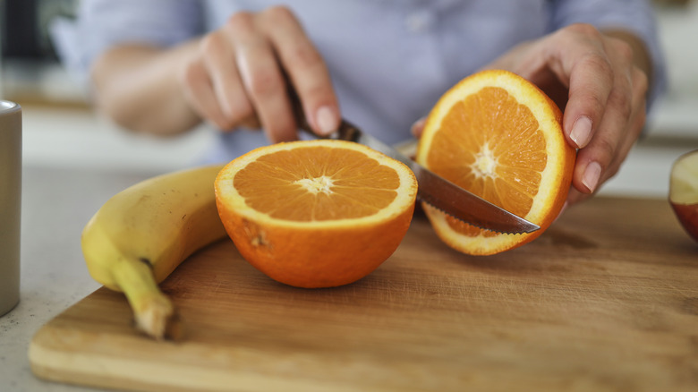 Person slicing orange next to banana