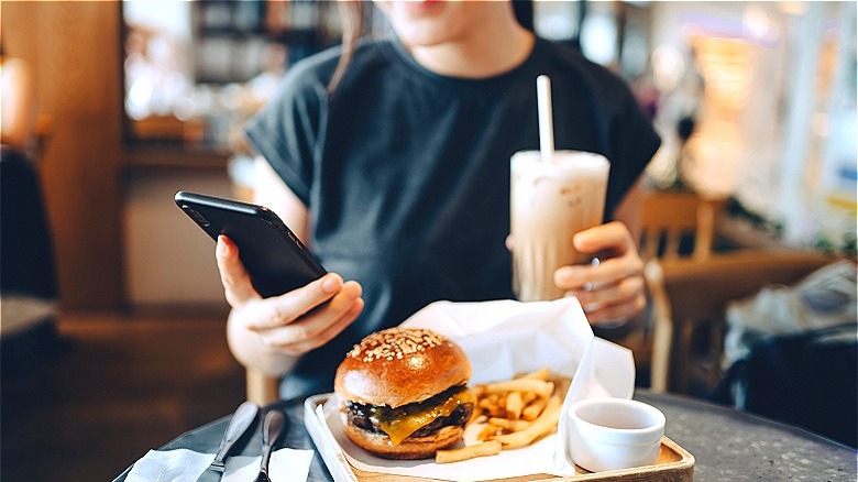 Person holding phone with food on table