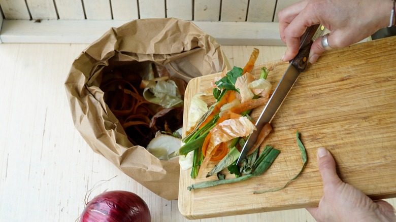 Knife scrapping vegetable scraps from board