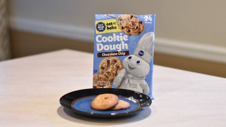 A package of Pillsbury chocolate chip cookie dough with two baked cookies on a blue and black plate