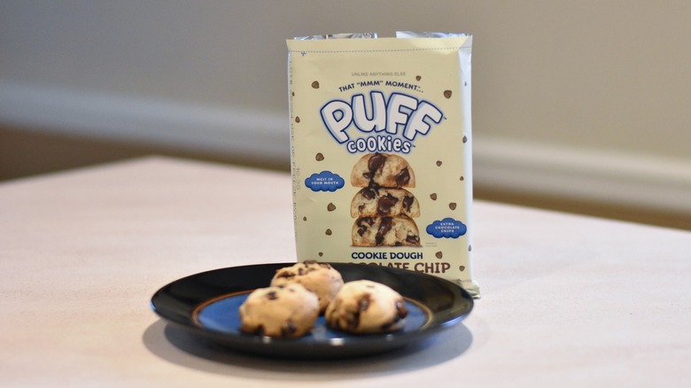 A package of Puff cookie dough with three baked cookies on a blue and black plate