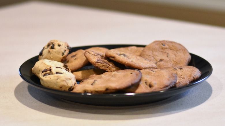 A plate of baked chocolate chip cookies of different sizes and shapes on a black plate