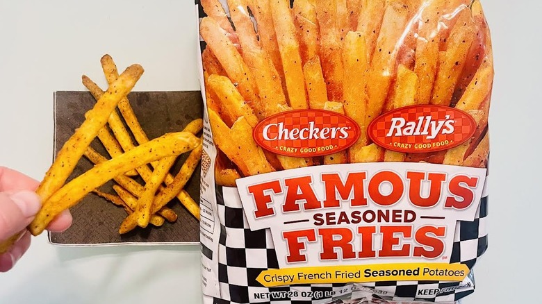 Bag of frozen Checkers/Rally's Famous Seasoned Fries with fingers holding cooked ones