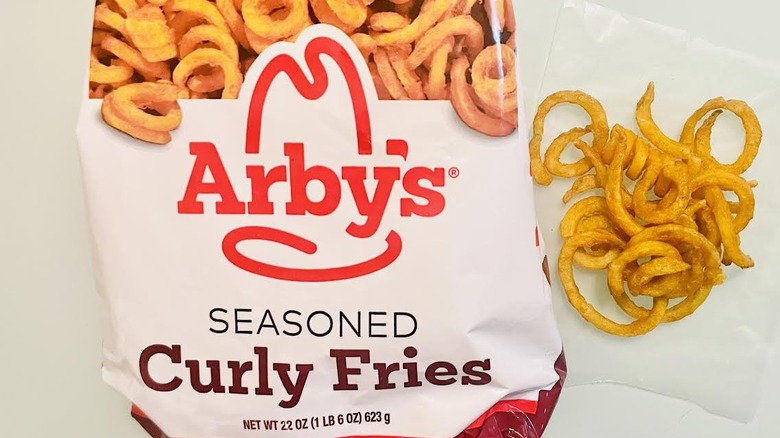 Bag of frozen Arby's Seasoned Curly Fries and cooked ones on the side