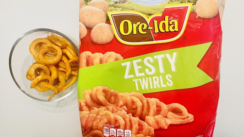 Bag of frozen Ore-Ida Zesty Curly Seasoned French Fries with mug of cooked ones