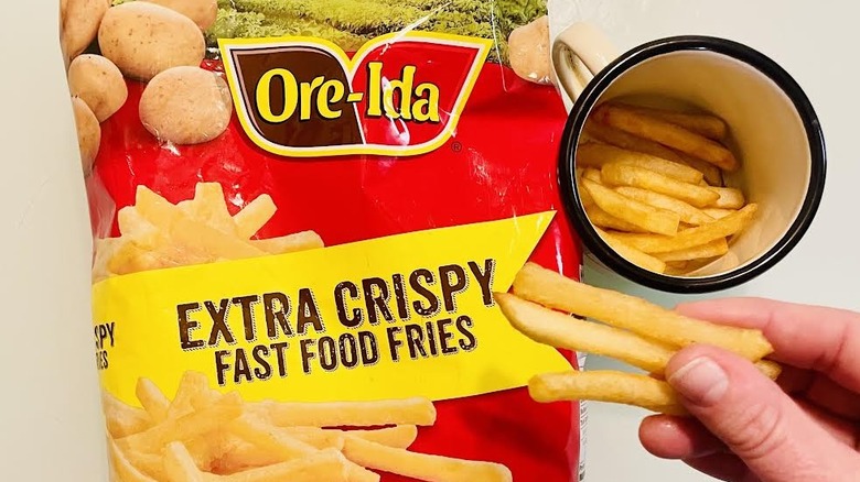 Bag of frozen Ore-Ida Extra Crispy Fast Food French Fries with hand holding cooked ones