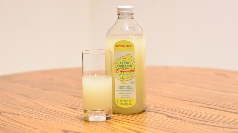 A bottle of Trader Joe's fresh squeezed lemonade next to a glass of lemonade