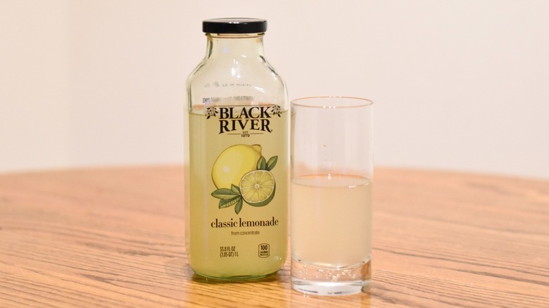 A jar of Black River classic lemonade next to a glass of lemonade on a wooden table