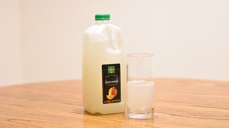 A jug of The Fresh Market fresh-squeezed lemonade next to a glass of lemonade