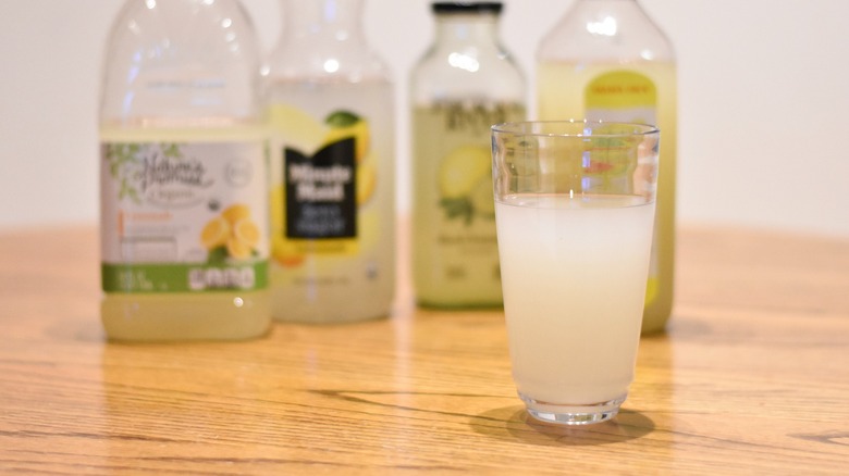 A glass of lemonade in front of lemonade bottles