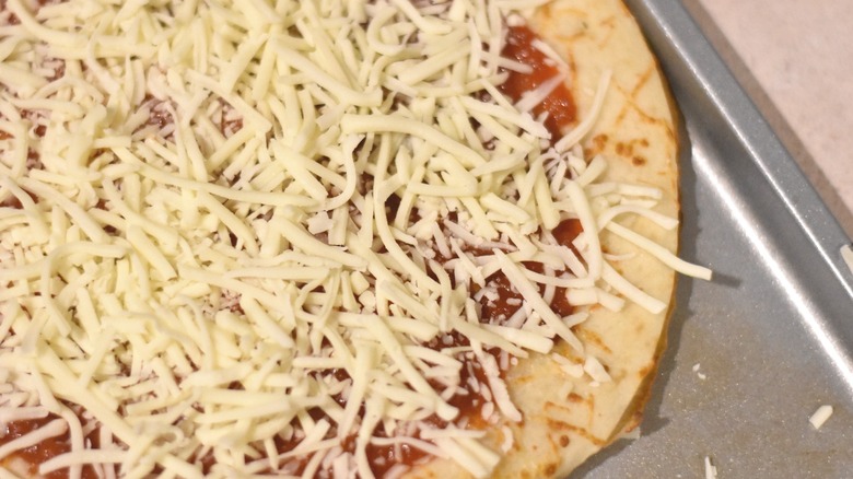 A prepared pizza crust with sauce and toppings on a baking sheet