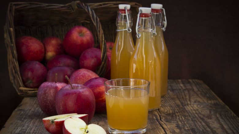 Bottles and a glass of fresh apple cider, with whole red apples in the background