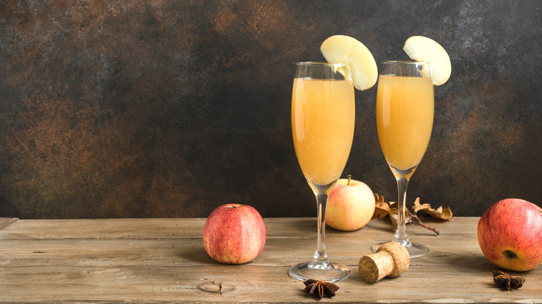 Two apple cider mimosas with an apple slice garnish on a wooden table