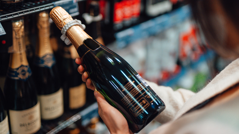 closeup of woman choosing bottle of champagne at store