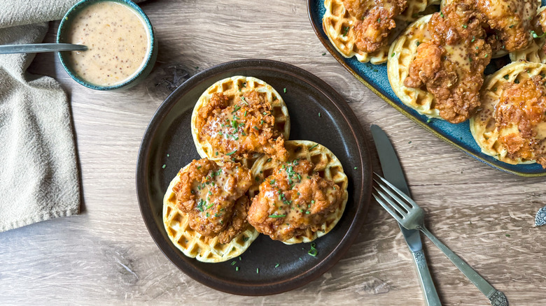 Sweet and savory crispy buttermilk chicken and waffles on plate and serving platter with spicy honey mustard sauce