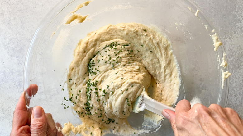 Folding chopped chives into waffle batter in glass bowl with spatula