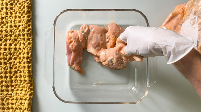 Removing chicken thighs from buttermilk brine to glass baking dish with latex glove